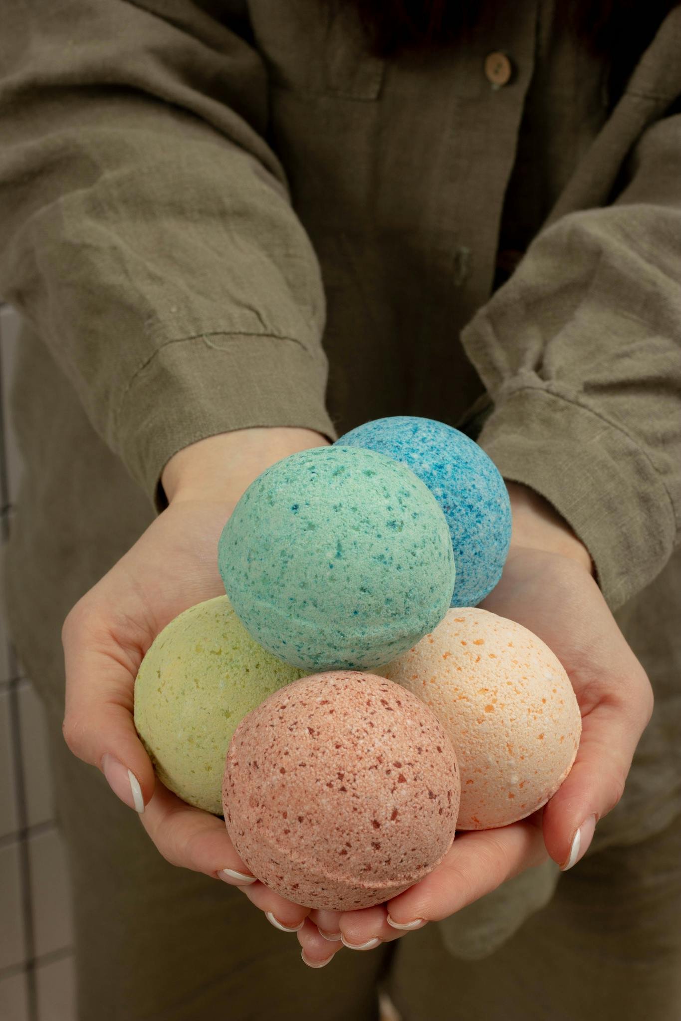 Contact us 1 Vibrant bath bombs in various colors held gently by a pair of hands, perfect for relaxing baths.
